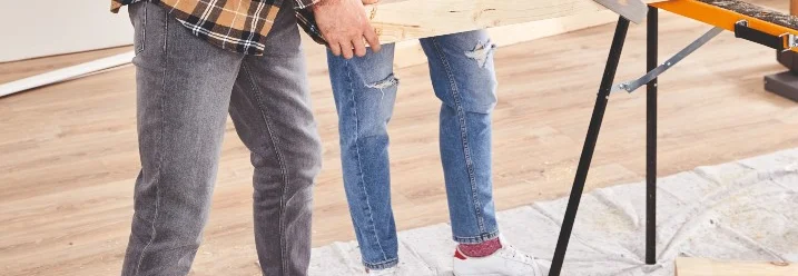 Zwei Personen sägen ein Kantholz mit einer Handsäge.